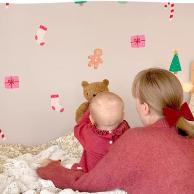Child sitting on a bed pointing at wall decals with holiday and nature themes.