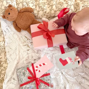 Baby sitting and looking at Christmas presents with red ribbons and Christmas cards.