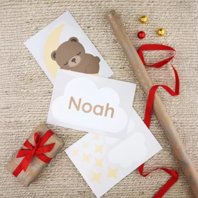 Door stickers on a sheet featuring a bear sleeping on a moon and a cloud that says “Noah,” surrounded by Christmas wrapping paper.