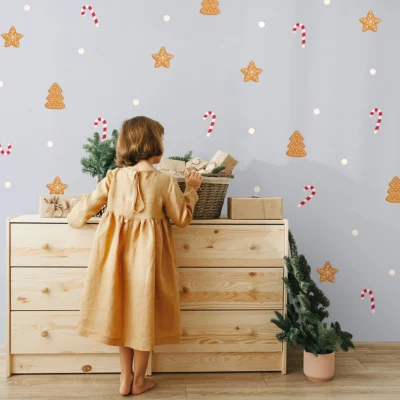 Wall décor with a Christmas motif featuring gingerbread cookies shaped like Christmas trees and stars, and candy canes, with a little girl in a dress standing in front of a dresser.