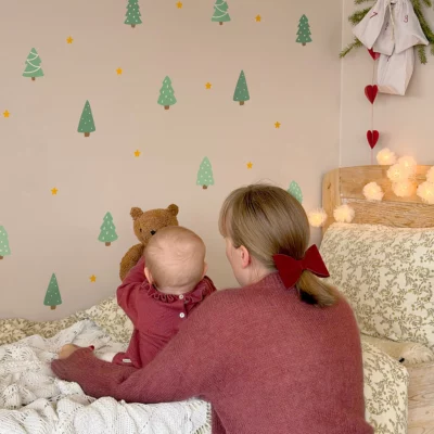 Child sitting on a bed pointing at wall decals with holiday and nature themes.