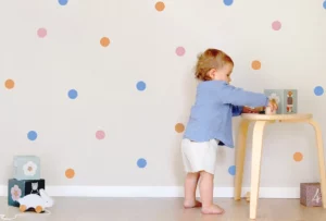 Child playing in a nursery with colorful polka dot wall decals.