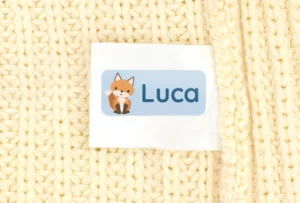 Personalized name label with fox design for children on a knitted fabric background.