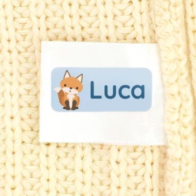 Personalized name label with fox design for children on a knitted fabric background.