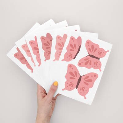 Hand holding multiple pink butterfly-themed decals.