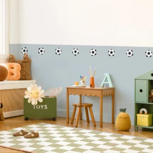 Alt-tekst: A children's room featuring playful wall decor with soccer ball motifs. The room includes a stylish wooden table with art supplies, a toy storage box labeled TOYS, and cozy seating. This vibrant space is perfect for kids and showcases the ideal environment for personalized name labels, children's wall art, and colorful posters.