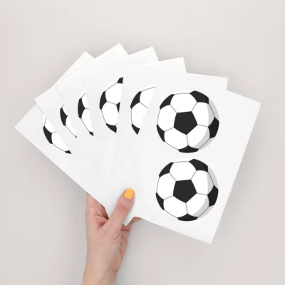 Alt-tekst: A hand holding multiple birthday cards featuring a soccer ball design, perfect for children's parties and themed celebrations. These cards can be customized with personal names to add a special touch to your child's birthday.