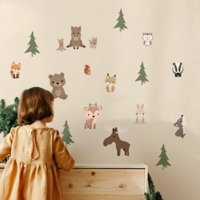 A young child admires playful woodland animal wall decals on a nursery wall, featuring bears, deer, and foxes, perfect for decorating children's rooms. Explore our collection of charming wall decor for kids to create a whimsical atmosphere.