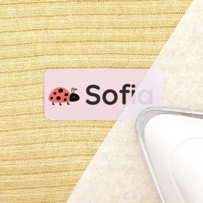 Personalized name tag featuring a ladybug design with the name Sofia, placed on a textured fabric background alongside an iron, ideal for home organization or children's items.