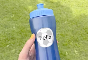 Personalized blue water bottle labeled with the name Felix and a soccer ball design, held against a green grass background. Ideal for sports activities and kids' use.