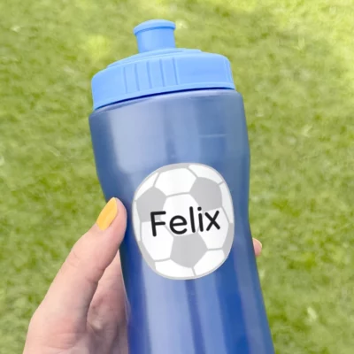 Personalized blue water bottle labeled with the name Felix and a soccer ball design, held against a green grass background. Ideal for sports activities and kids' use.
