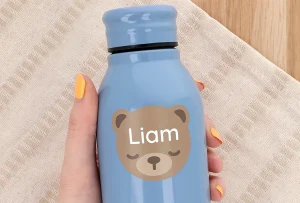 Personalized blue water bottle featuring a cute bear design and the name Liam. Handheld against a textured background, highlighting its child-friendly aesthetic and customizability. Ideal for children's hydration needs or as a unique gift.