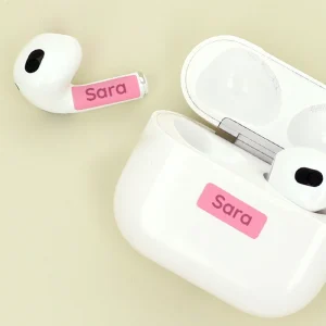 Personalized name tags on wireless earbuds and charging case, featuring the name Sara on a pink background, ideal for easy identification and organization.