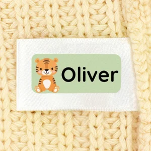 Custom name tag featuring the name Oliver alongside a cute tiger illustration, displayed on a textured beige fabric background. Ideal for personalizing children's belongings.